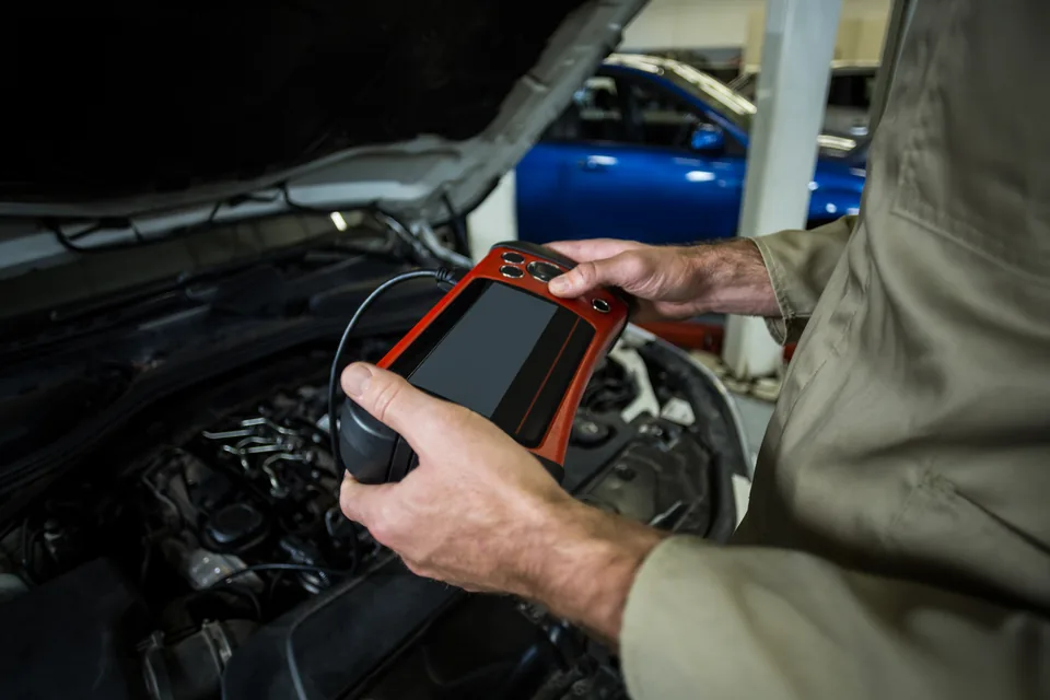 Mechanic using a diagnostic tablet beside an open engine bay