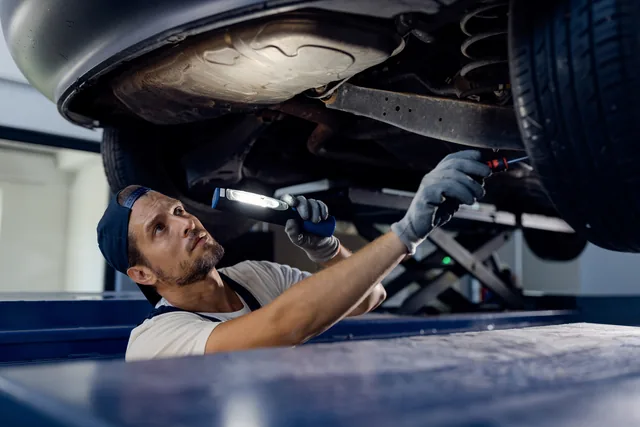 Mechanic inspecting the underside of a raised vehicle with a torch